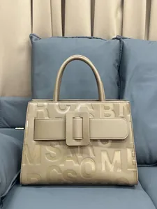 Detail of beige tote bag featuring embossed letters and a large square buckle accent
