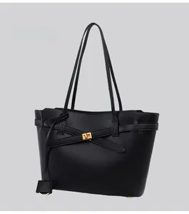 Detail of black leather tote bag featuring a gold metal twist lock and cross strap design