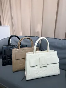 Three textured faux leather tote bags with embossed letters on a grey sofa