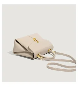 Close-up of beige lychee grain leather handbag with gold metal lock and side pleats