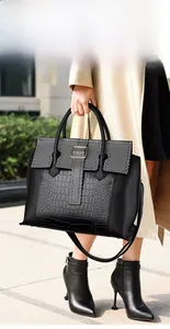Close-up of black tote bag featuring textured faux crocodile skin and metallic buckles