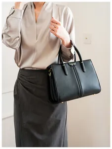 Close-up of Muse Bag black leather tote with gold logo and elegant curved handle