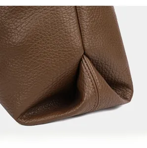 Macro view of brown lychee leather tote bag showing pleated corners and neat stitching