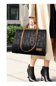 Detail of a large textured tote bag featuring embossed letters and brown leather tag
