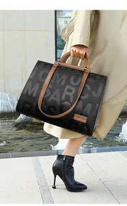 Detail of black tote bag with embossed lettering and contrasting brown leather handles