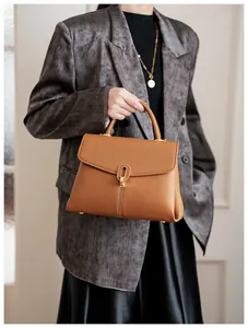Detail view of brown lychee grain leather handbag with gold metal lock on a gray suit