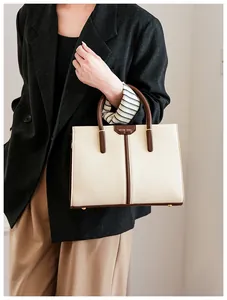 Detail of a structured cream handbag with brown handles and a gold MUSE BAG logo plate