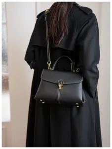 Detail of black pebbled leather texture with white stitching and gold hardware on handbag