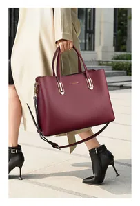 Close-up of wine red leather tote with gold hardware and grain texture on a street