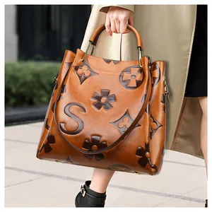Detail of caramel brown tote bag with luxury embossed patterns and golden metal hardware