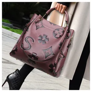 Close-up of a burgundy leather bucket bag with embossed monogram patterns and metal handles