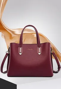 Detail of burgundy pebbled leather handbag with gold logo and elegant silk backdrop