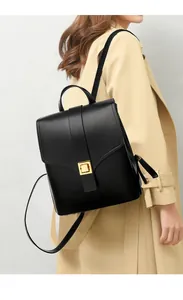 Side view of black matte leather backpack on beige trench coat showing gold square buckle