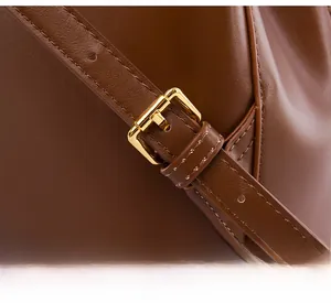 Close-up of brown leather shoulder strap with gold metal buckle and neat stitching