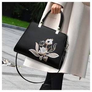Dettaglio del ricamo floreale sulla borsa in pelle nera con finiture metalliche oro
