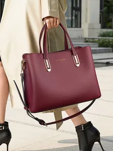 Elegant wine red leather tote bag with gold hardware shown in a street style view