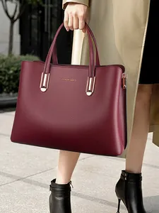 Burgundy grain leather tote bag with gold hardware held by a model in a trench coat
