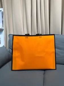 Detalle de una bolsa de compras premium naranja y negra sobre un sofá de cuero gris