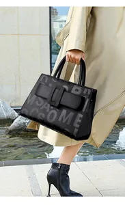 Outdoor street style shot of a black leather tote bag with embossed grey artistic letters