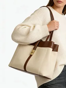 Detail of cream canvas tote bag with brown leather trim and golden twist lock closure