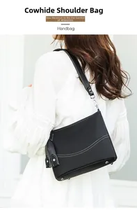 Close-up of black cowhide shoulder bag with white contrast stitching on a female model