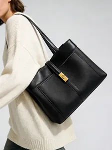 Detail of black tote bag with cross pattern leather and gold metal buckle on white sweater