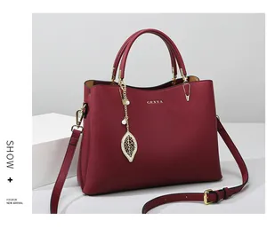 Detail van de bordeauxrode leren handtas met gouden hanger en logo op een witte standaard