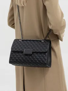 Bolso bandolera acolchado negro con cadena plateada y negra sobre abrigo camel