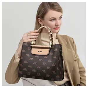 Detail of woven gold handle and brand logo on a brown printed tote bag with metal flap