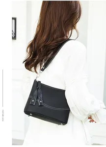 Detail of black pebbled leather crossbody bag with white stitching and tassel charm