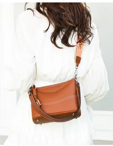 Brown leather crossbody bag with wide patterned strap and fringe detail on white dress