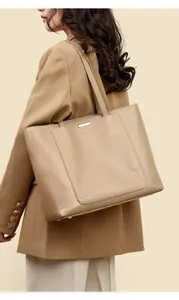 Detail view of large beige tote bag with litchi texture and gold bar on model shoulder