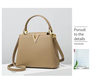 Detail of light brown lychee grain leather handbag with gold V-shaped metal hardware