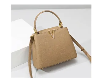 Macro shot of litchi grain beige leather handbag featuring a gold V-shaped metal logo buckle