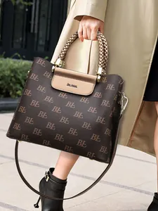 Brown monogram tote bag with braided handle and long strap worn by a woman in a coat
