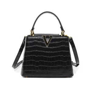 Detail of black crocodile texture handbag with gold V-shaped metal logo and hardware
