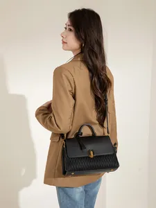 Detail of black wave pleated leather tote bag with gold metal buckle on brown blazer