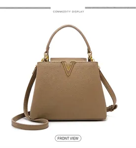 Close-up of tan lychee leather handbag featuring a prominent golden V-shaped metal buckle