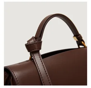 Close-up of brown leather handbag featuring knotted handle and gold metal hardware detail