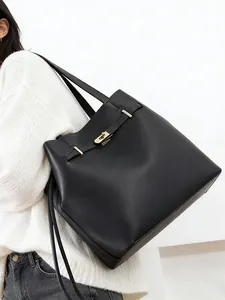 Detailed view of black leather tote bag with gold buckle on a model wearing white sweater