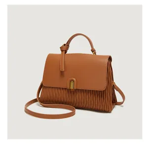 Detail of caramel brown handbag featuring pleated leather texture and a metal lock clasp