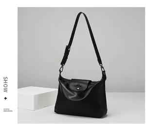 Detail of black faux leather tote bag featuring a metal M logo buckle and adjustable strap