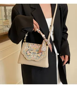 Close-up of beige crossbody bag featuring floral embroidery and silk scarf handle detail