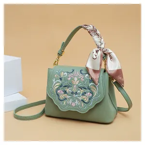 Close-up of vintage floral embroidery on sage green leather handbag with silk scarf handle