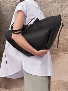 Bolso tote minimalista de cuero negro con cordón lateral mostrado en modelo