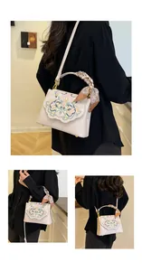 Close-up of floral embroidery on a white leather crossbody bag with a silk scarf handle