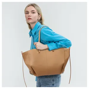 Detalle de un bolso tote grande de cuero marrón con asas largas sobre camisa azul