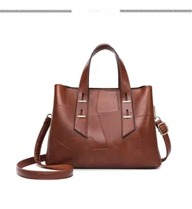 Detail of a brown leather tote bag showing unique patchwork design and golden hardware