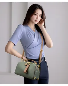 Dettaglio borsa Boston in pelle verde scuro con manici marroni e finiture dorate
