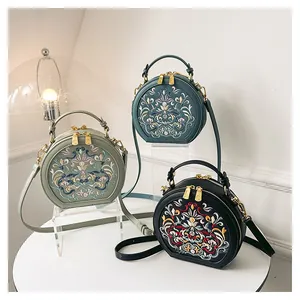 Close-up of vintage round crossbody bag with floral embroidery and gold zippers